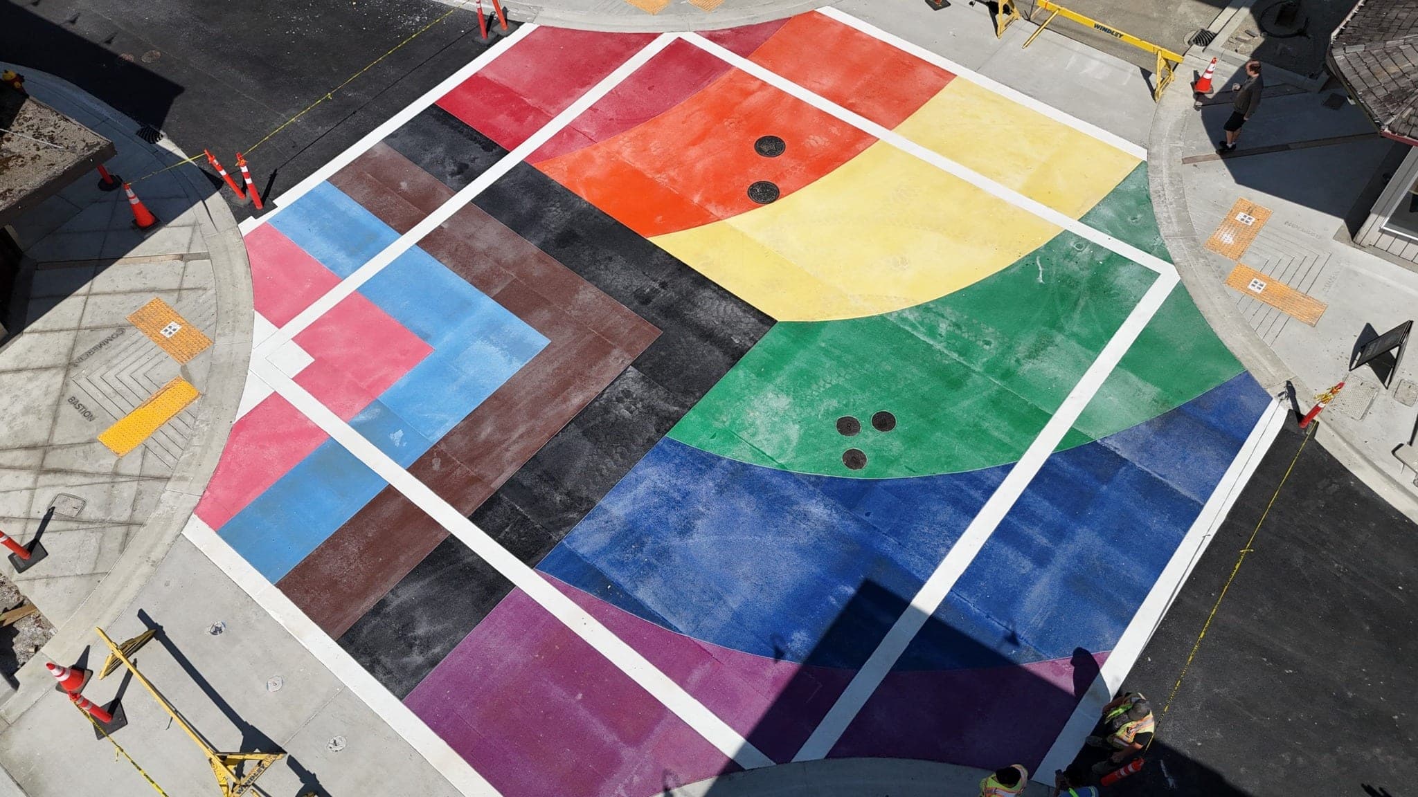 The rainbow intersection in Nanaimo from above — the whole crossing in bands of red, orange, yellow, green, blue and purple TrafficPatternsXD, installed by Square One Paving