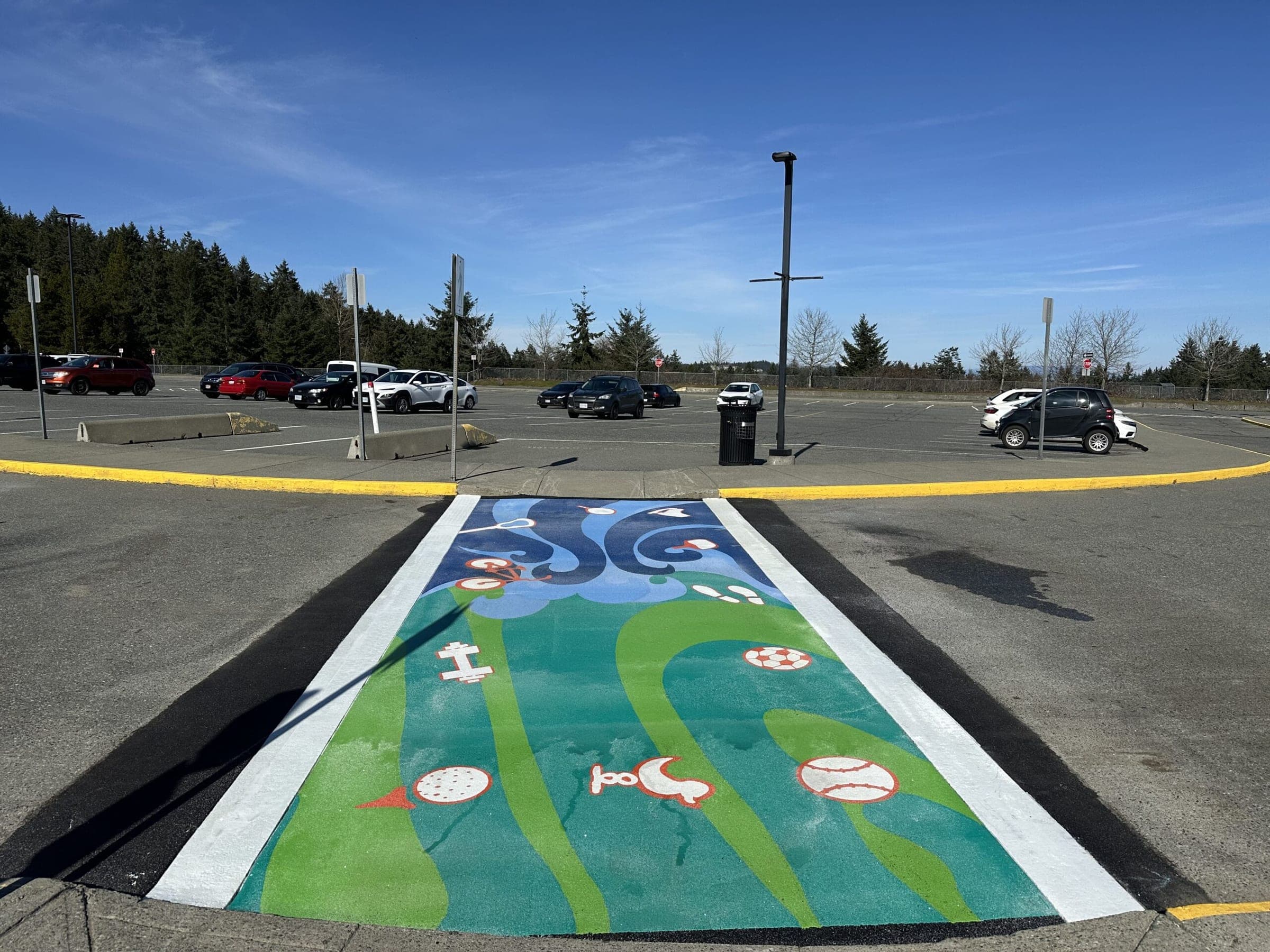 A sports-themed TrafficPatterns crosswalk across the Beban Park lot in Nanaimo, a soccer ball, a baseball, a golf ball and a bicycle set in green and blue waves, installed by Square One