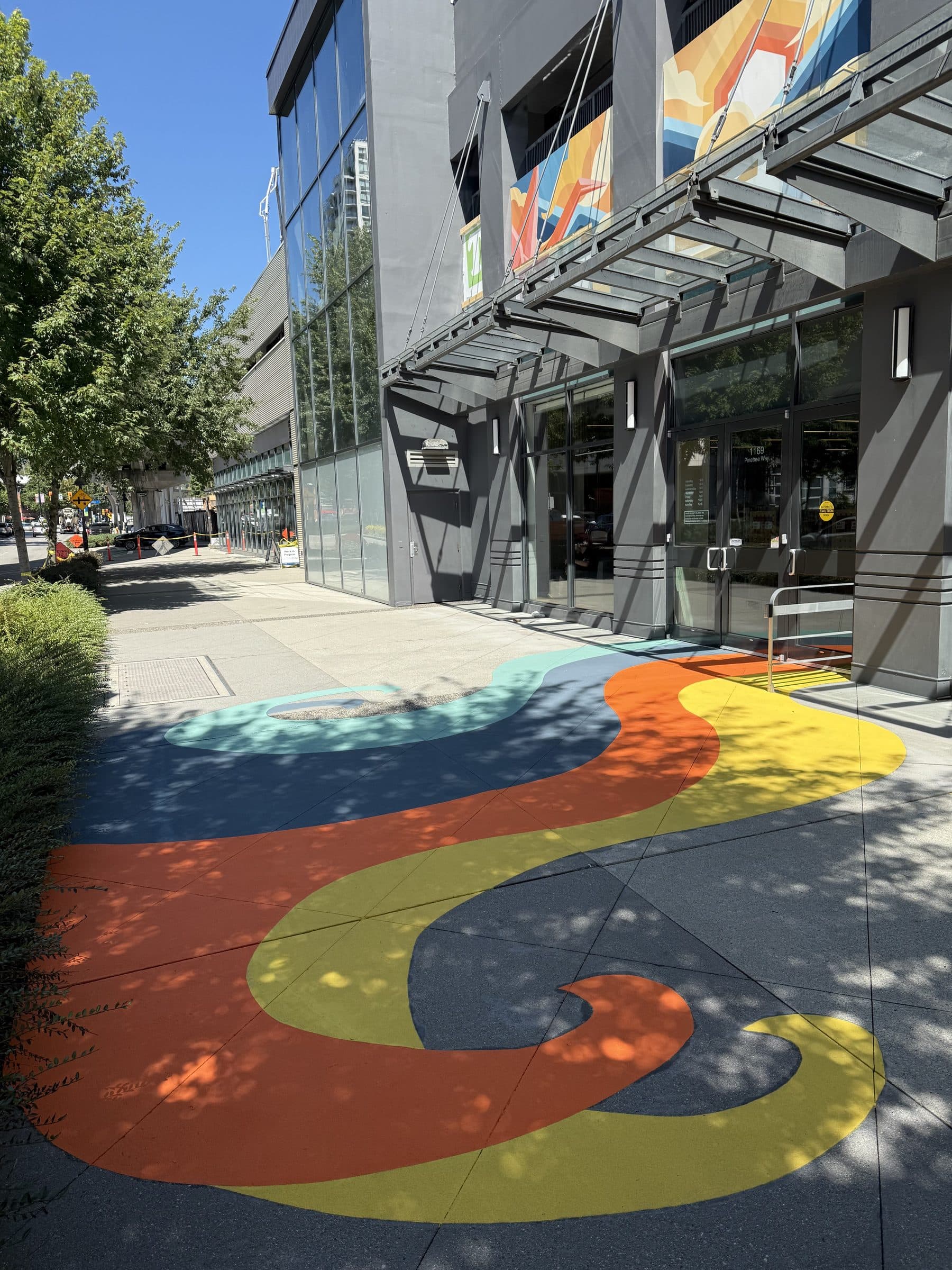 Bands of teal, blue, orange and yellow StreetBond sweeping along a retail plaza sidewalk in Coquitlam