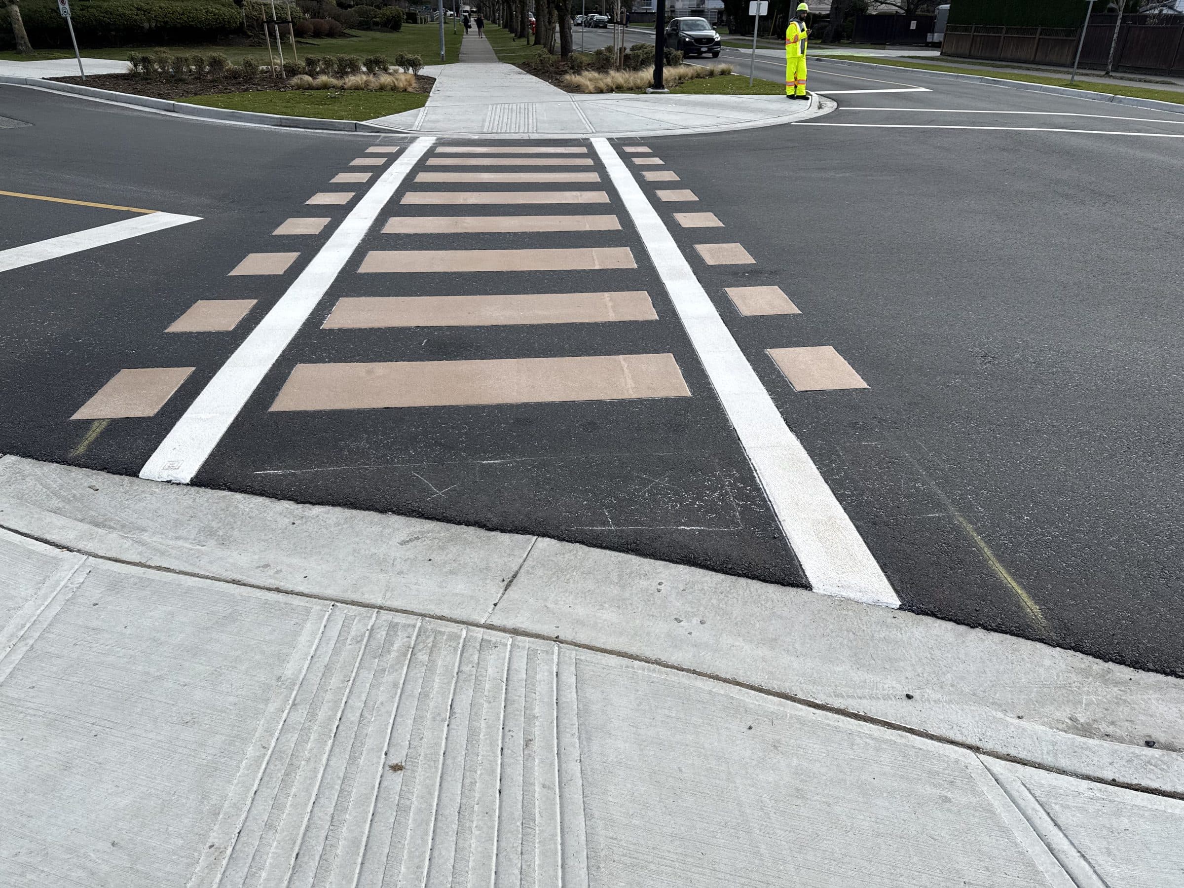 A railway-tie pattern TrafficPatternsXD crossing in tan and white running across a wide intersection in Langley, a flagger in high-visibility gear at the far corner