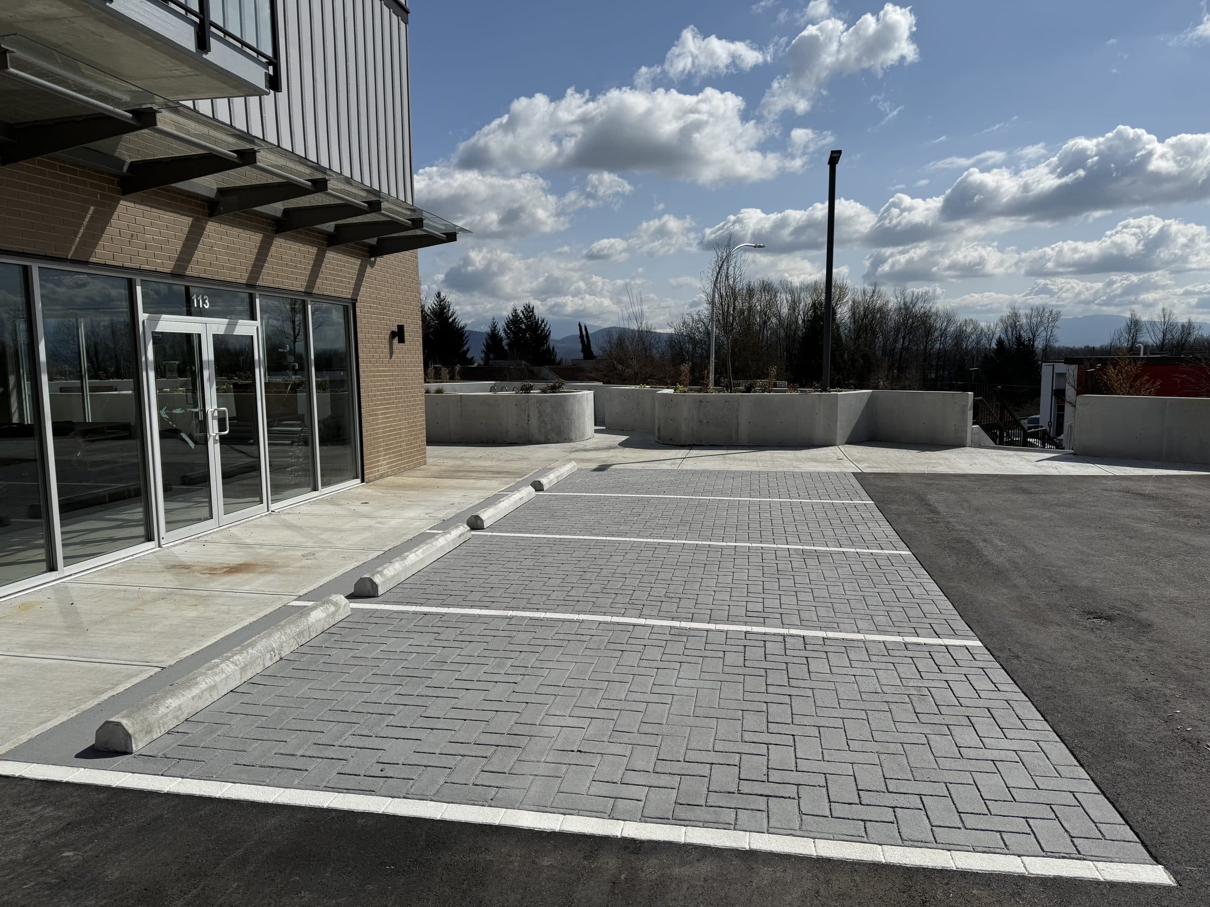 Grey herringbone StreetPrint parking bays in front of a new commercial building in Mission, clouds over the hills beyond, installed by Square One