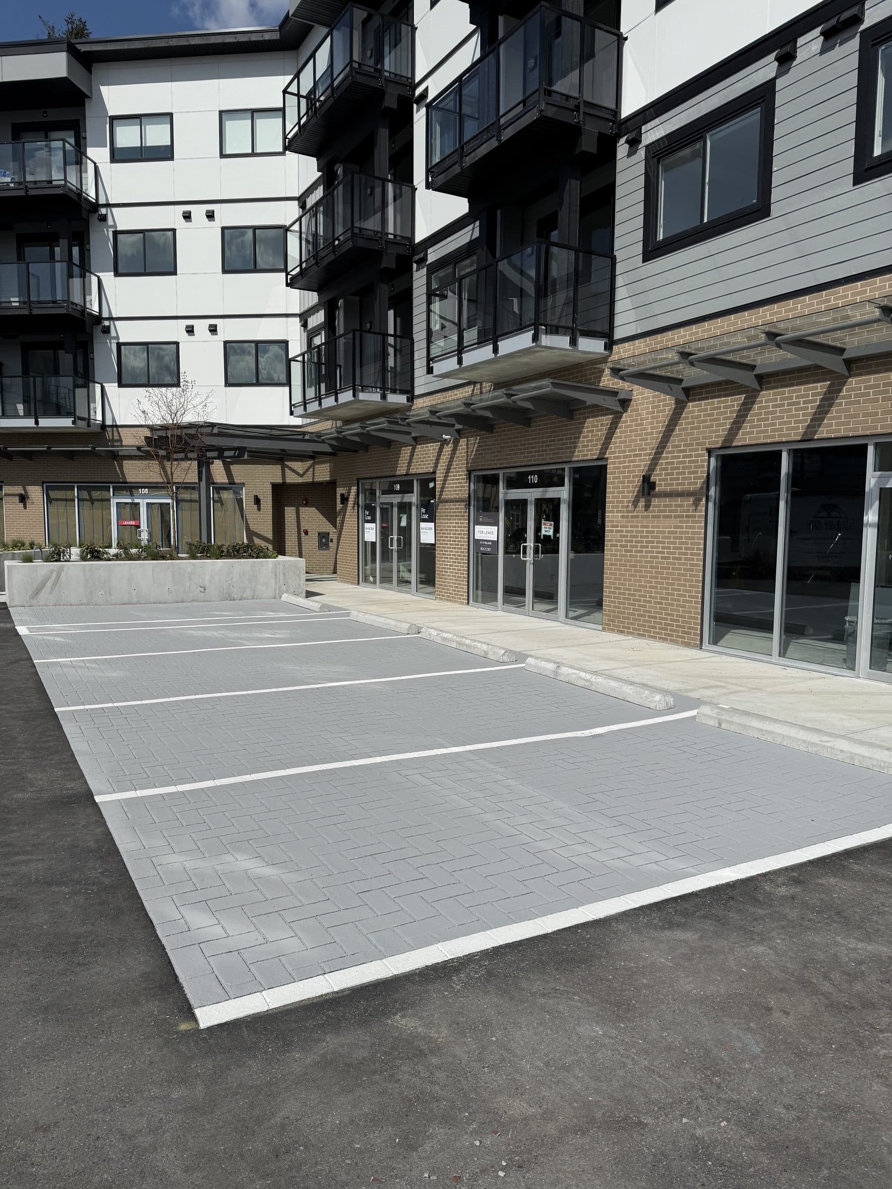 Grey herringbone StreetPrint parking bays along the glass shopfronts of a new building in Mission