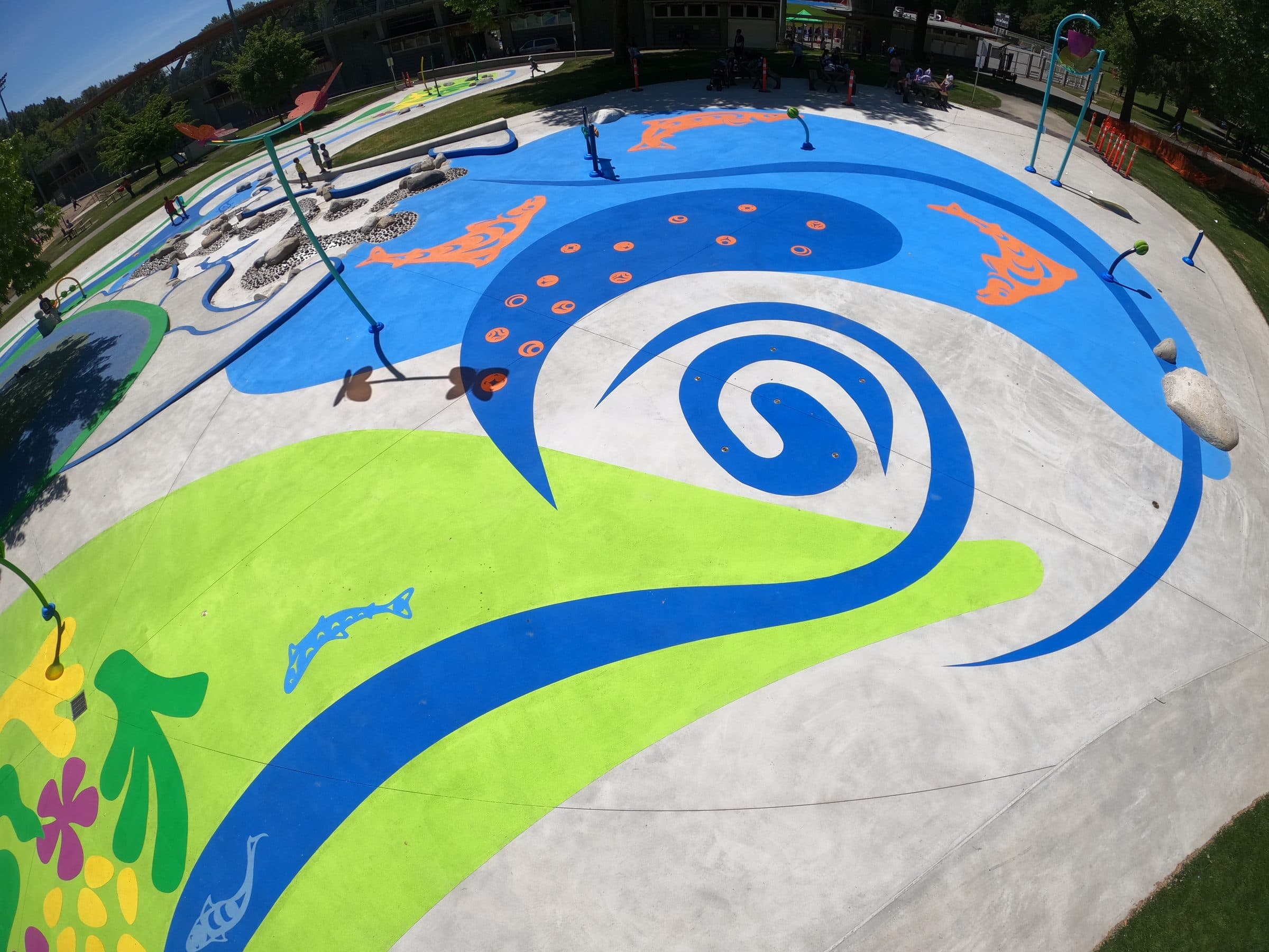 A marine spray park in Surrey, a swirl of blue StreetBond water through lime-green and yellow leaf shapes, orange fish in the current, installed by Square One
