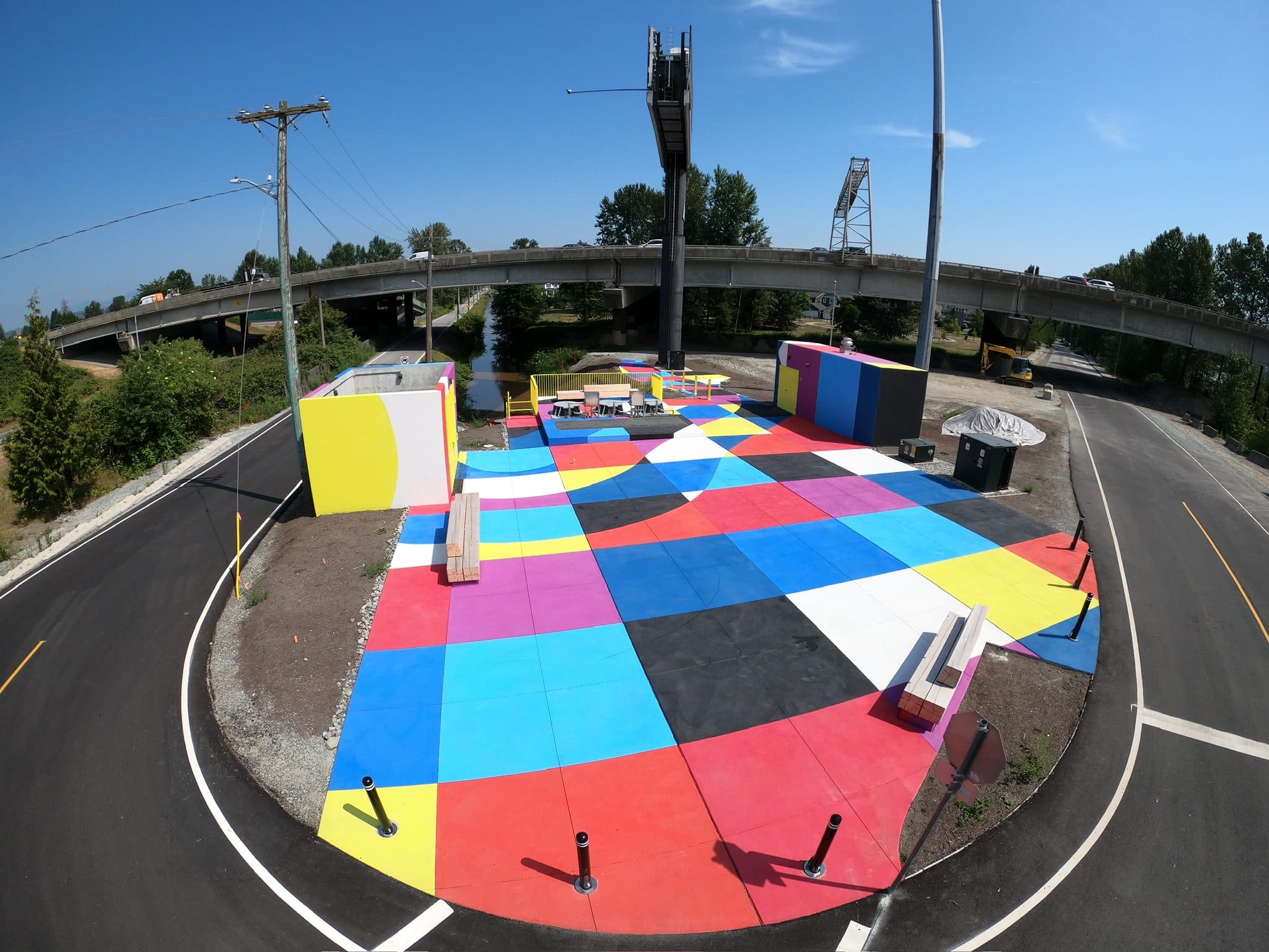 The Boundary Road pump station plaza in New Westminster — a quilt of red, blue, yellow, pink, black and white StreetBond squares under the SkyTrain guideway, installed by Square One