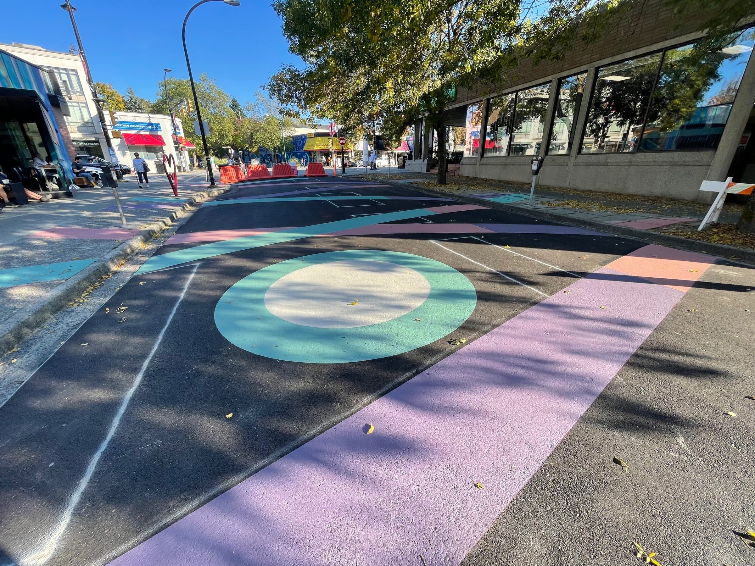 A StreetBond street mural in green, cream, lilac and red rolling across the crossing at 18th and Cambie, Vancouver, on a sunny afternoon