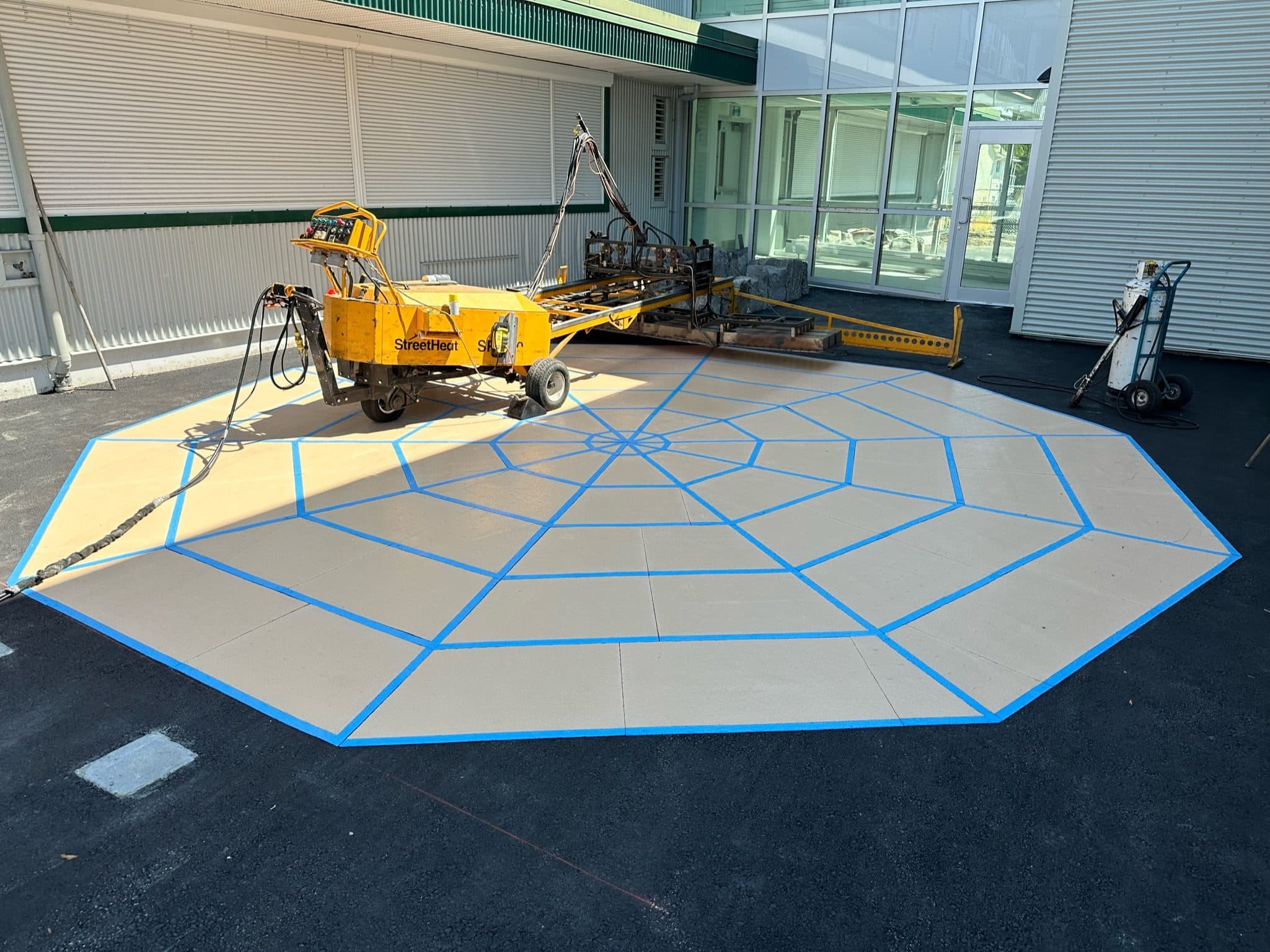 The infrared heater rig parked on a freshly laid grey octagon with blue web lines mid-install at KB Woodward school, Surrey