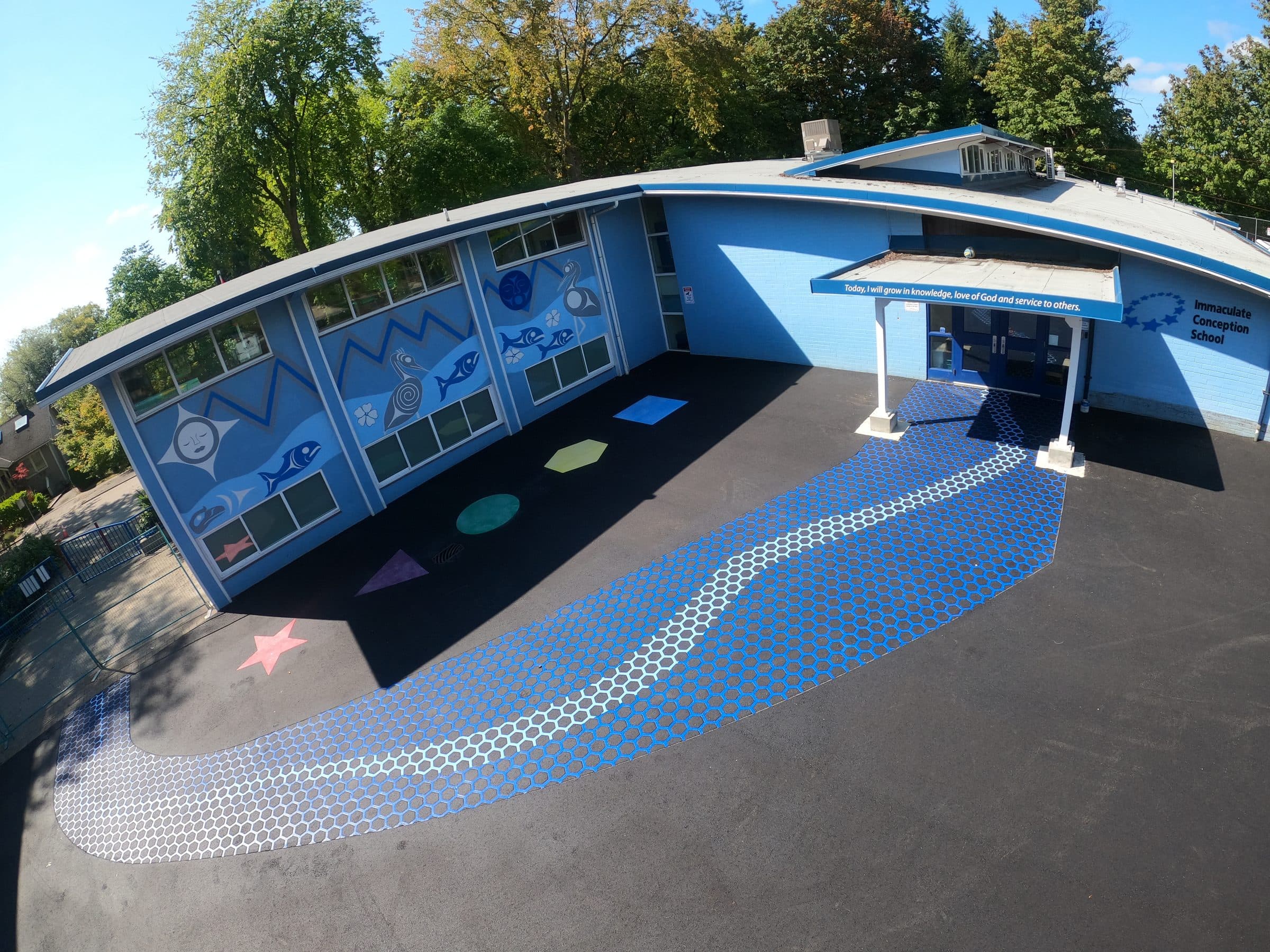 A path of blue StreetBond hexagons running across a school playground in Vancouver to the front doors, stars and shapes set around it