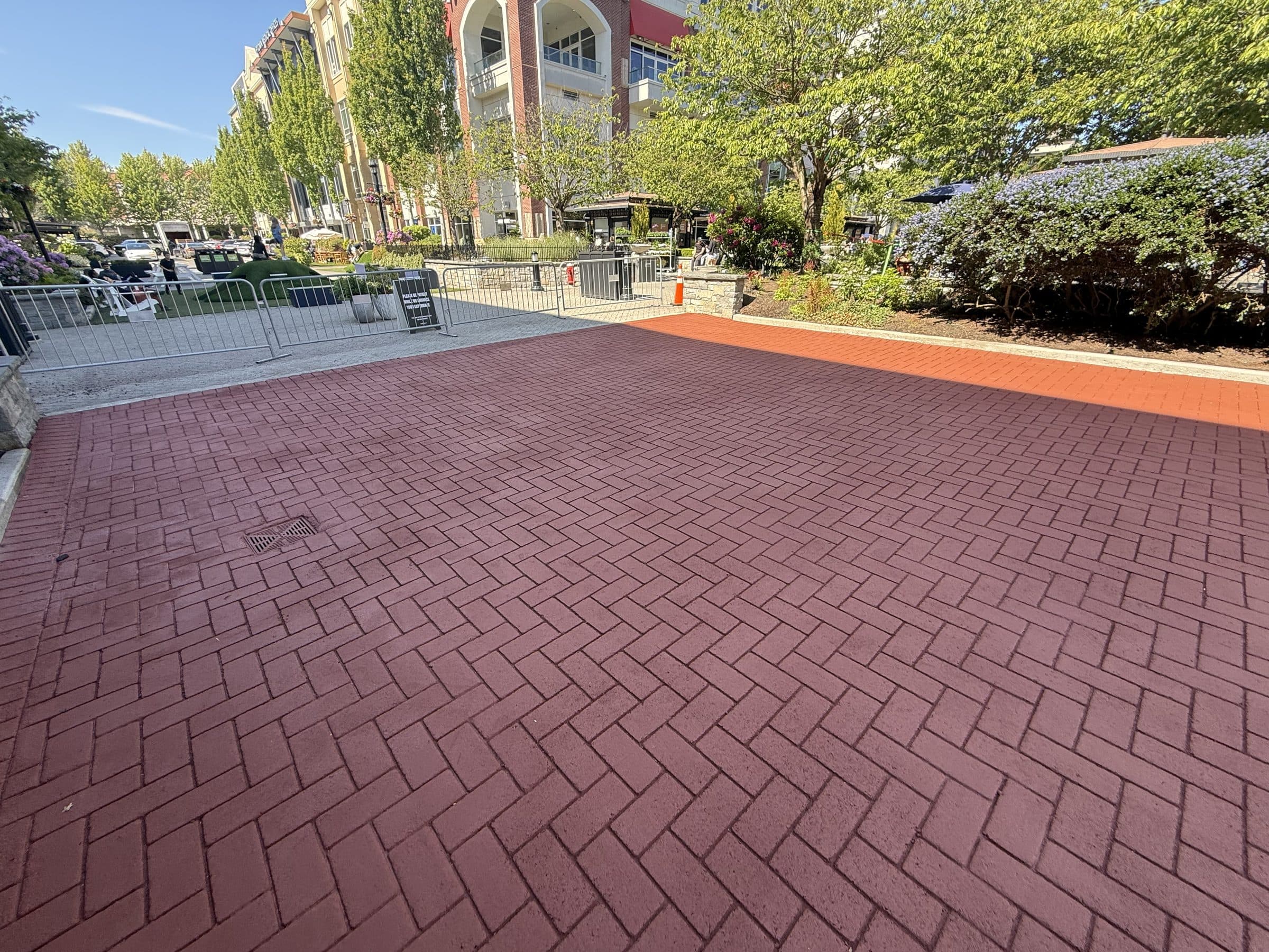 Brick-red herringbone StreetPrint stamped asphalt paving a town centre plaza in Victoria, with benches, trees and shopfronts beyond