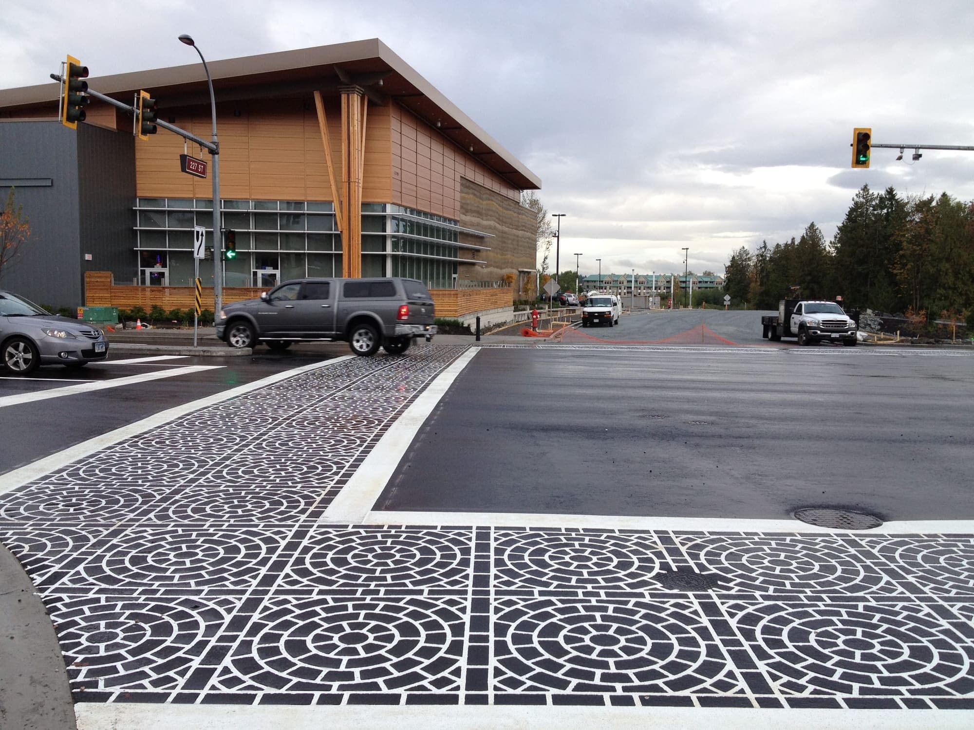 Black and white circle-pattern DuraTherm crosswalks meeting at a signalled intersection in Maple Ridge, wet after rain