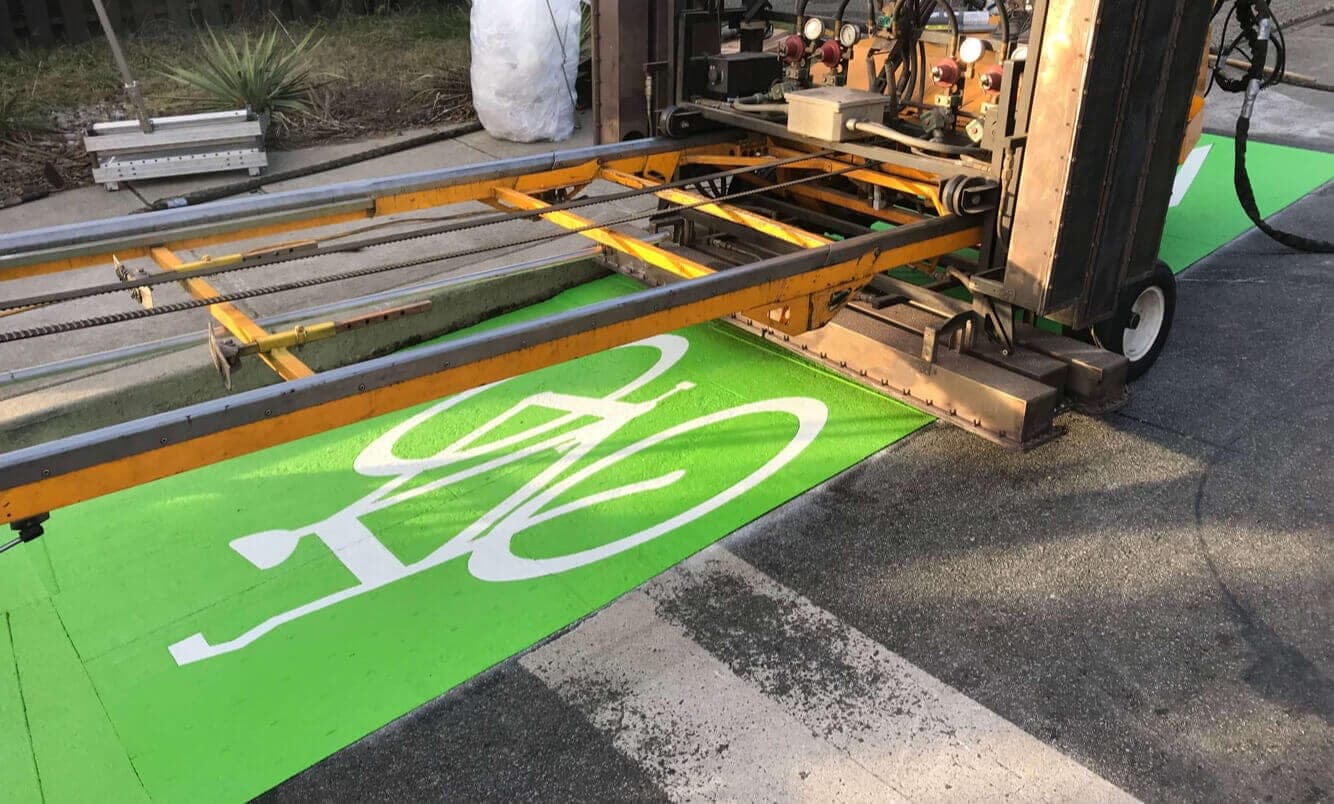 A white bicycle symbol in PreMark preformed thermoplastic being heat-applied to a green bike lane in North Vancouver, the heater rig over the marking