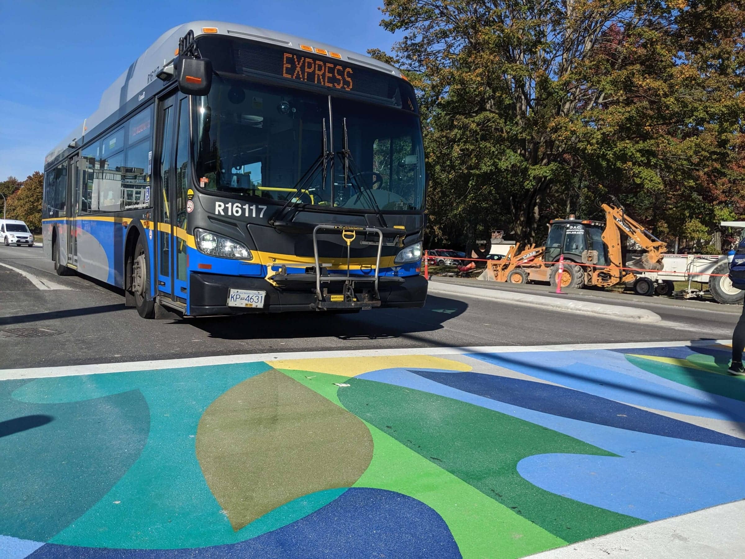 A bus crossing the blue and green TrafficPatterns crosswalk of the UBC and Musqueam crests at University Boulevard, Vancouver